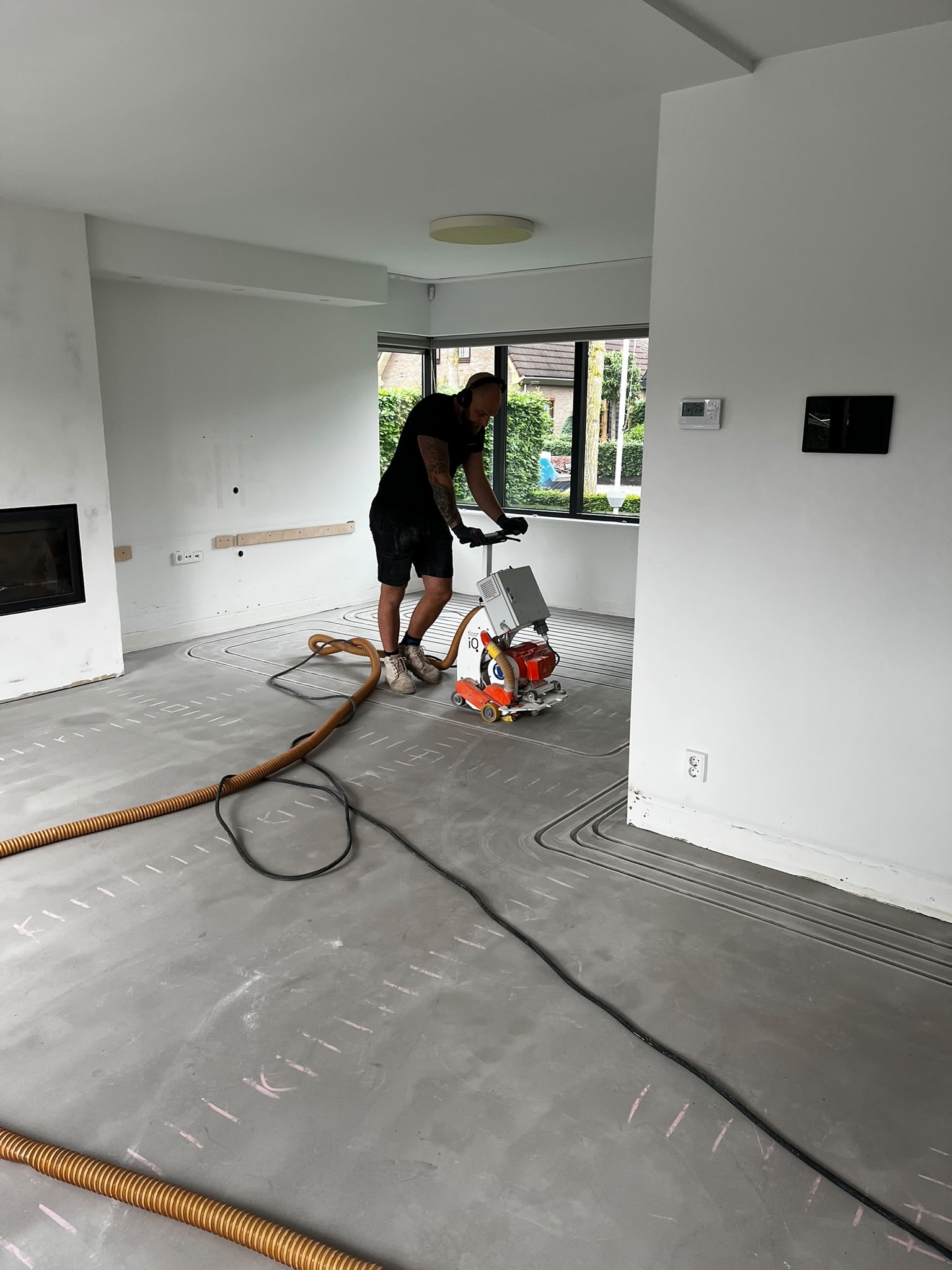 Angelo aan het werk met een vloerfrees en afzuigslang in een witte woonkamer