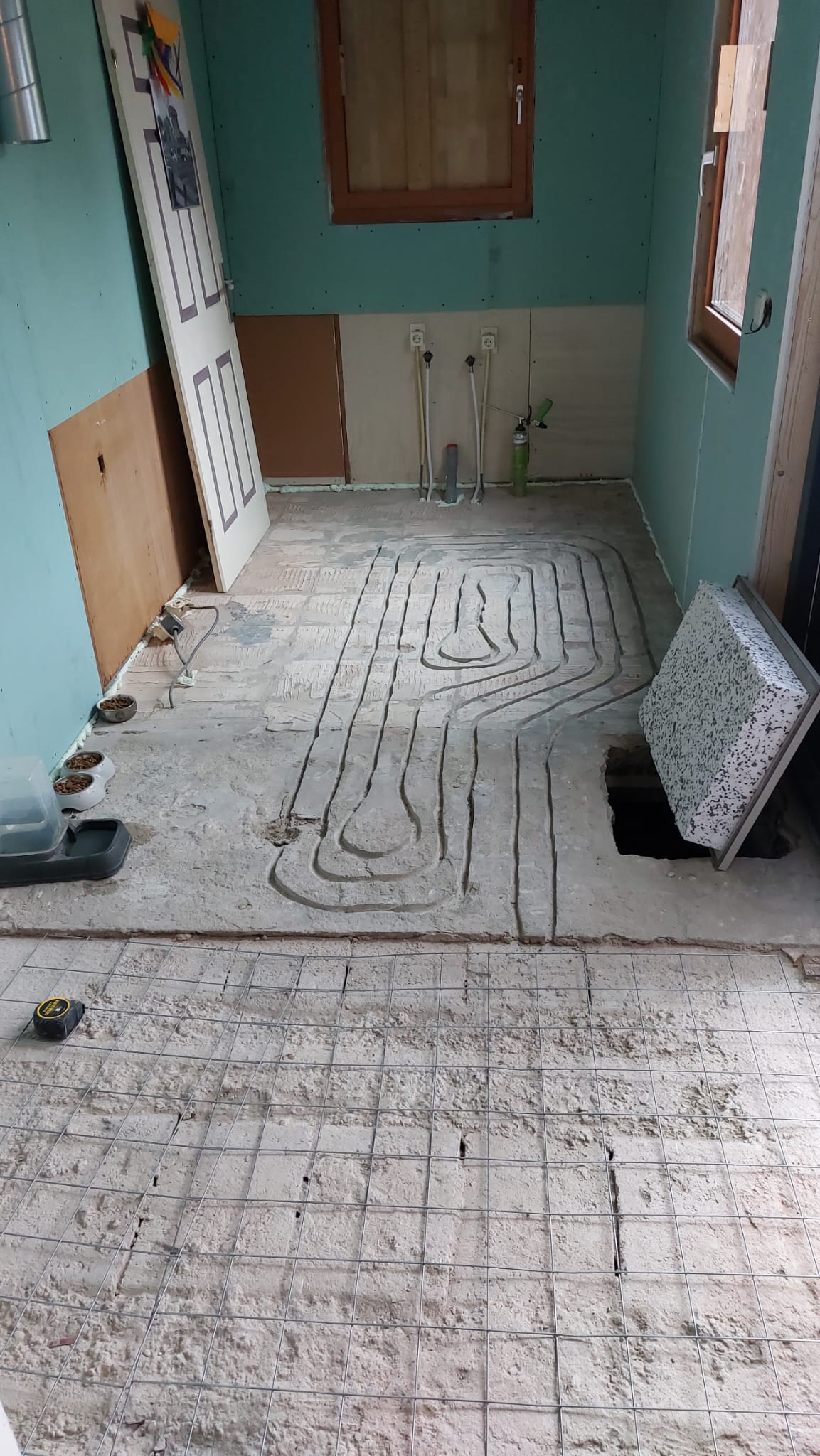 Gefreesde lussen met vloerverwarmingsbuizen in de vloer bij de keuken, met een turquoise wand