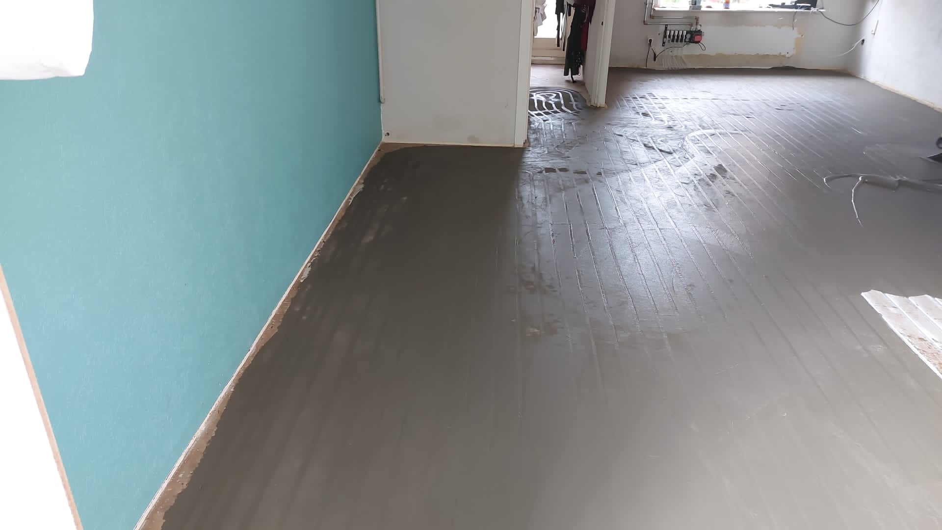 Dezelfde vloer na het afsmeren, glad en grijs langs de turquoise wand
